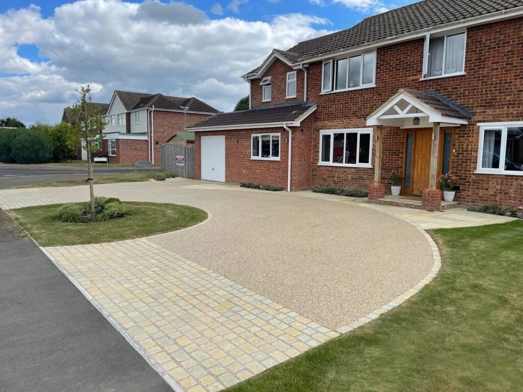 A picturesque brick house with a landscaped driveway, featuring a round gravel area and neat grass patches under a cloudy sky.
