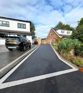 A newly paved driveway leads between two houses, with a parked black SUV on one side and greenery along the path.