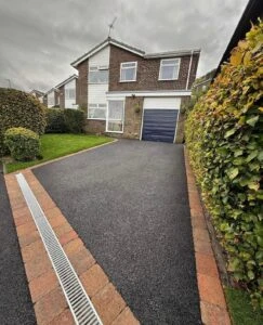 A two-story house with a driveway lined with bricks, surrounded by hedges, under a cloudy sky.