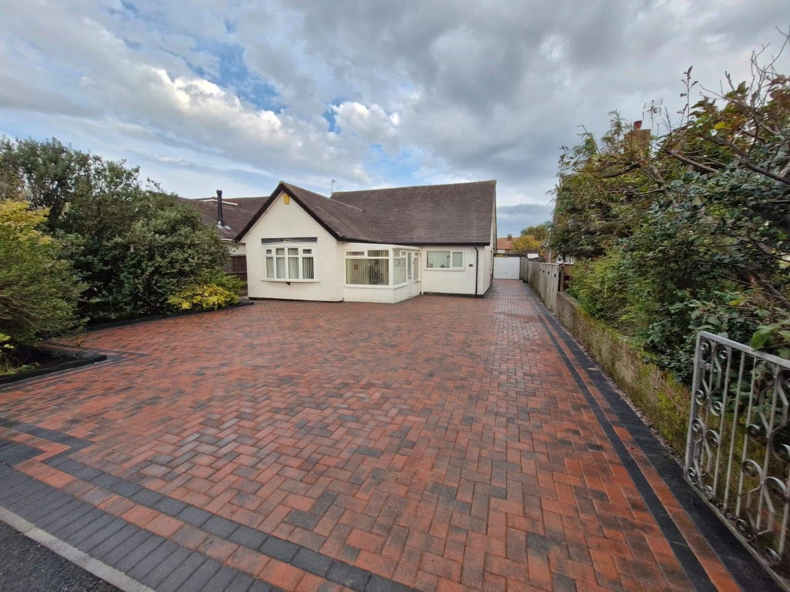 A residential home with a paved driveway, surrounded by greenery under a cloudy sky.