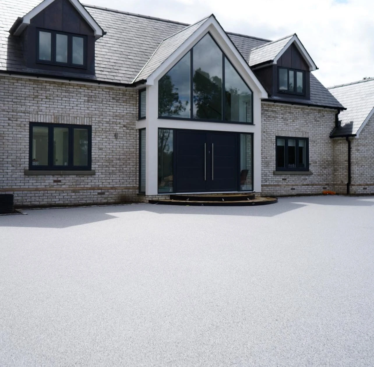 Modern house facade with large glass entrance and elegant stone exterior, featuring a white surface in front.