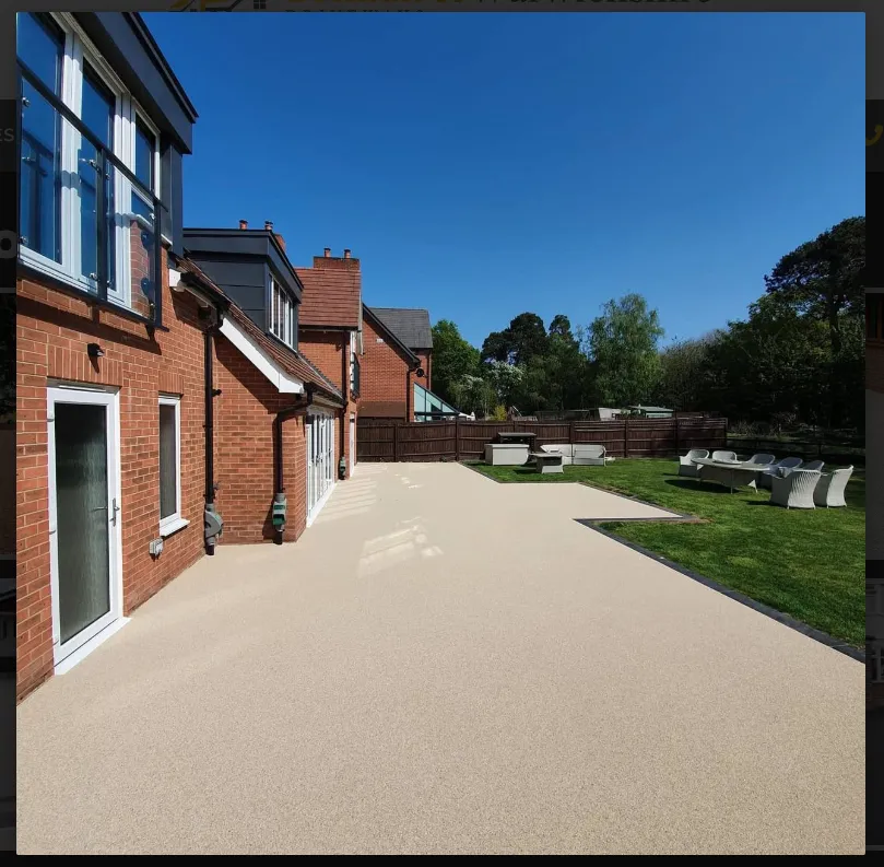 Backyard view featuring a smooth, light-colored patio, green lawn, and modern outdoor furniture under a clear blue sky.